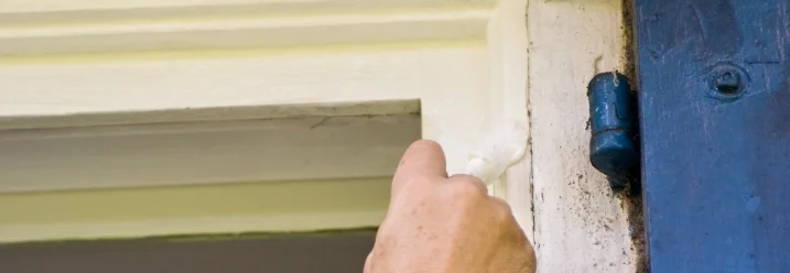 Person streicht Fensterrahmen weiß